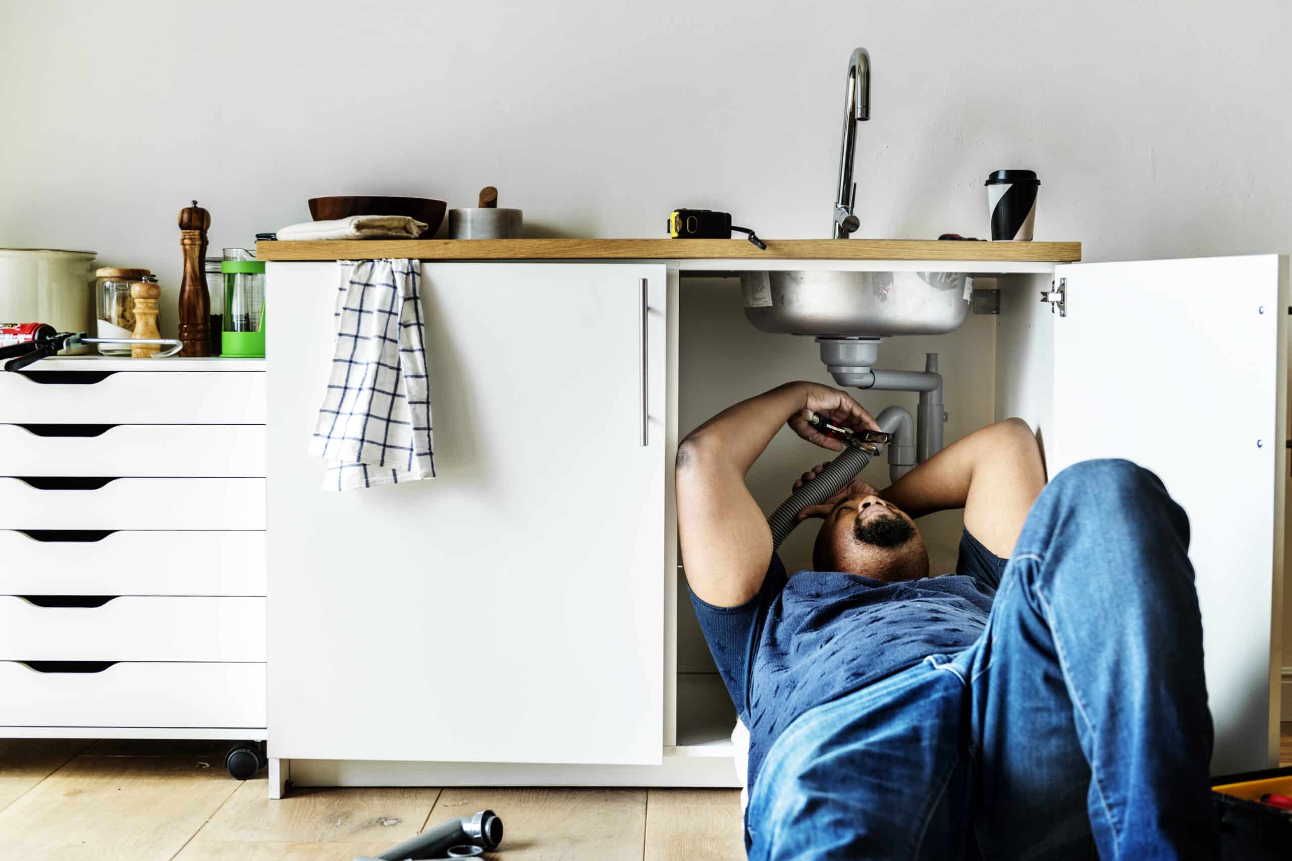 Plumber fixing a garbage disposal unit mounted under a kitchen sink