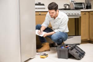 Technician doing a work report on a refrigerator in a home kitchen, illustrating a noise diagnosis