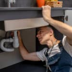 Technician inspecting the plumbing under a kitchen sink, illustrating garbage disposal troubleshooting