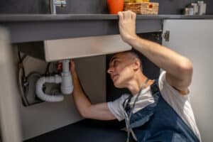Technician inspecting the plumbing under a kitchen sink, illustrating garbage disposal troubleshooting