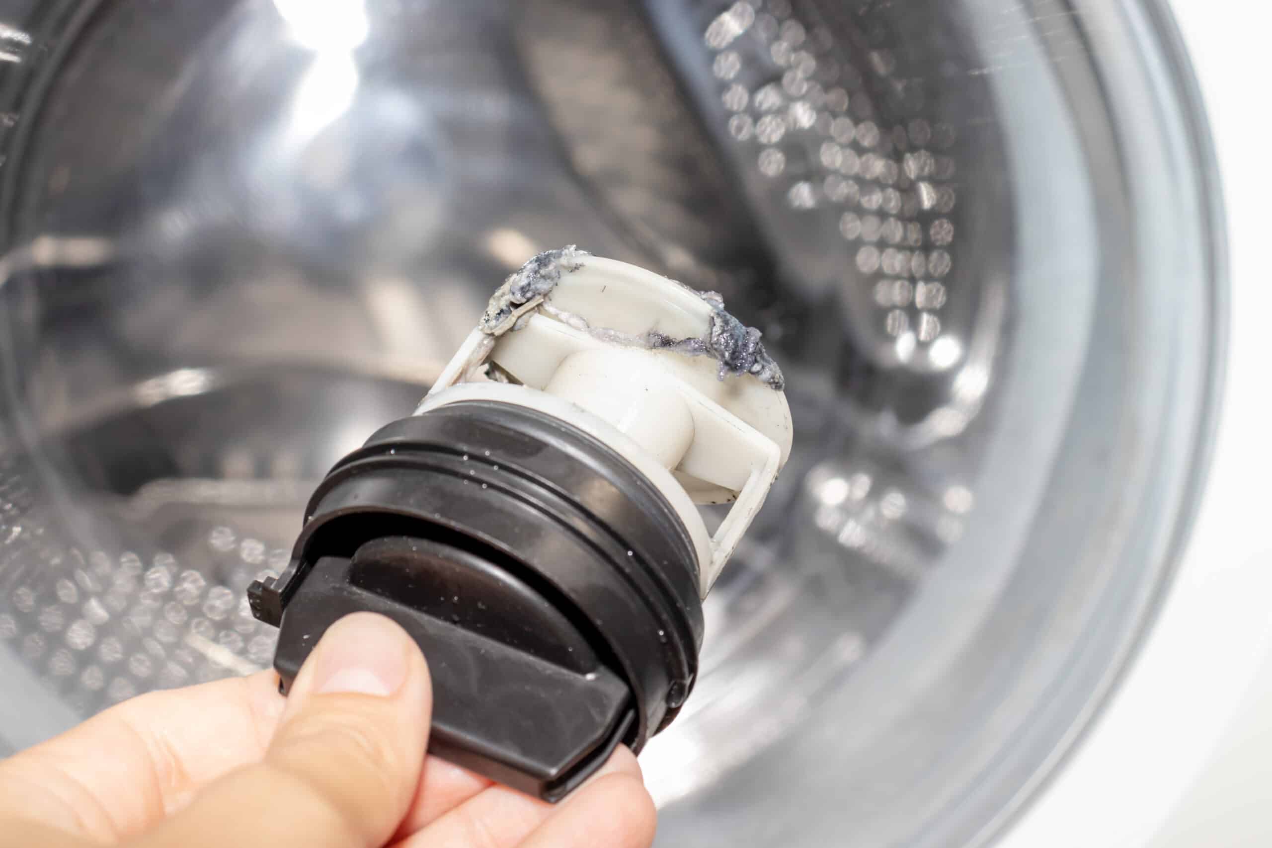 Technician inspecting a clogged washing machine drain pump filter to fix OE drain error