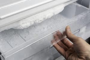 Hand opening a freezer drawer showing heavy frost buildup on the evaporator