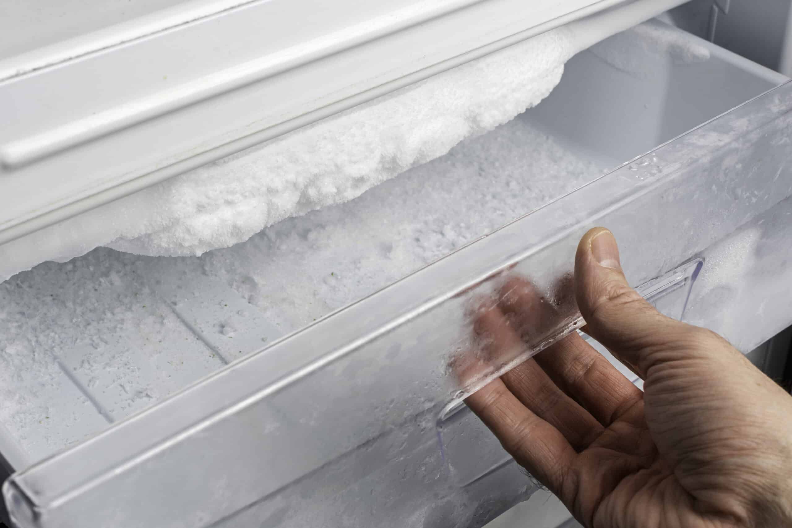 Hand opening a freezer drawer showing heavy frost buildup on the evaporator