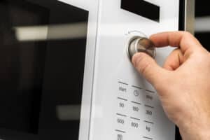 Hand pressing a button on a microwave oven keypad