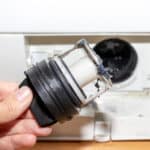 Close-up of a washing machine's dirty drain pump filter being cleaned
