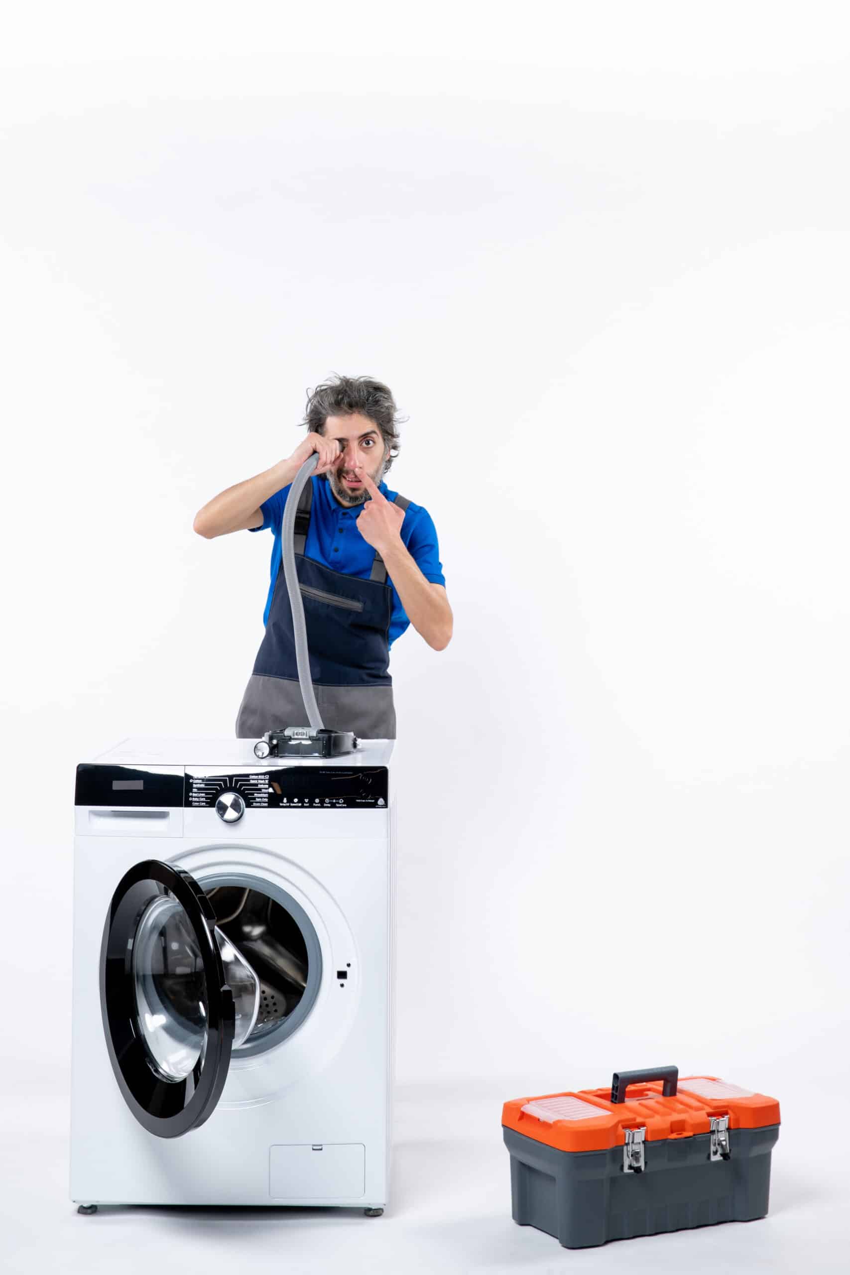 Repairman in uniform pointing at a pipe behind a washing machine, illustrating Whirlpool washer error code FP drain fault