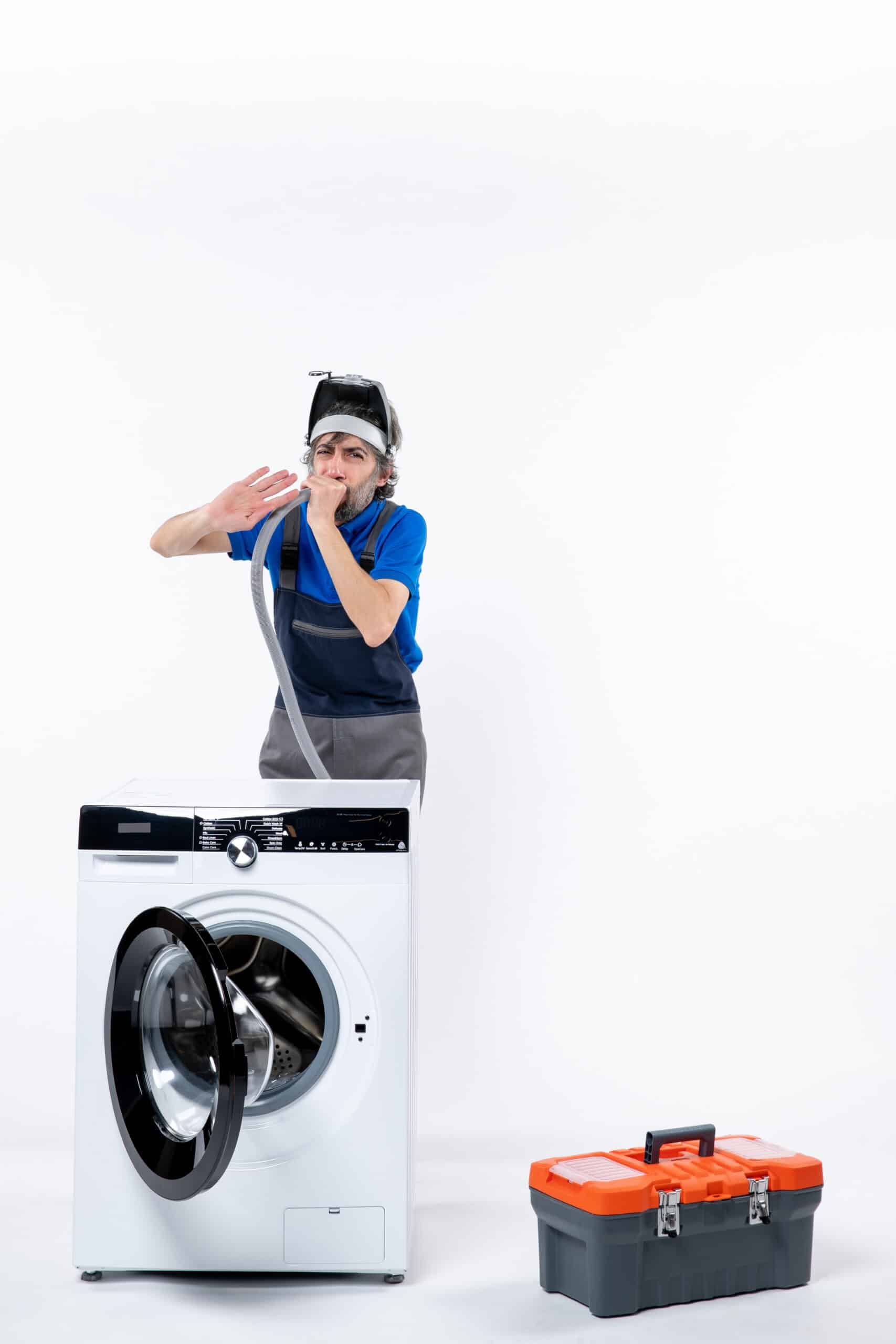 Repairman with a head lamp clearing a pipe behind a washing machine, illustrating Whirlpool washer FP drain fault error code