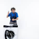 Repair technician pointing at a front-load washing machine while diagnosing a GE washer E2 drain error