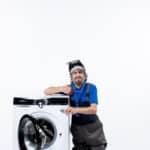 Repairman sitting near a washing machine, illustrating Whirlpool washer F22 error code motor communication fault
