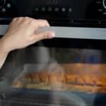 Hand opening an oven door, showing the door latch and lock mechanism area
