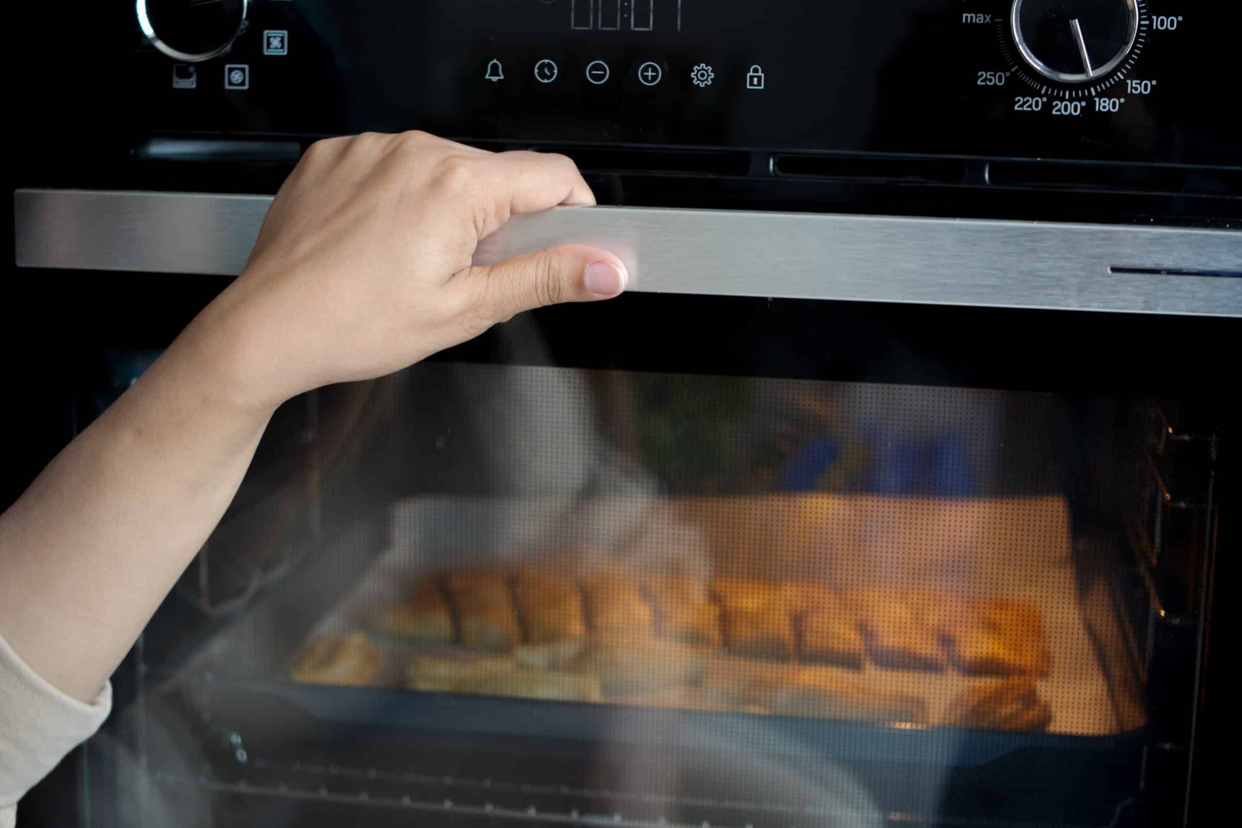 Hand opening an oven door, showing the door latch and lock mechanism area