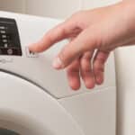 Main appuyant sur le bouton d'un lave-linge blanc