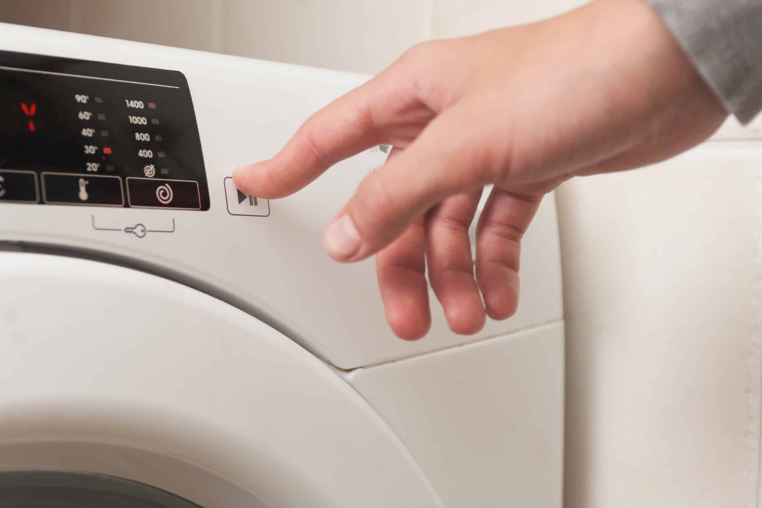 Main appuyant sur le bouton d'un lave-linge blanc