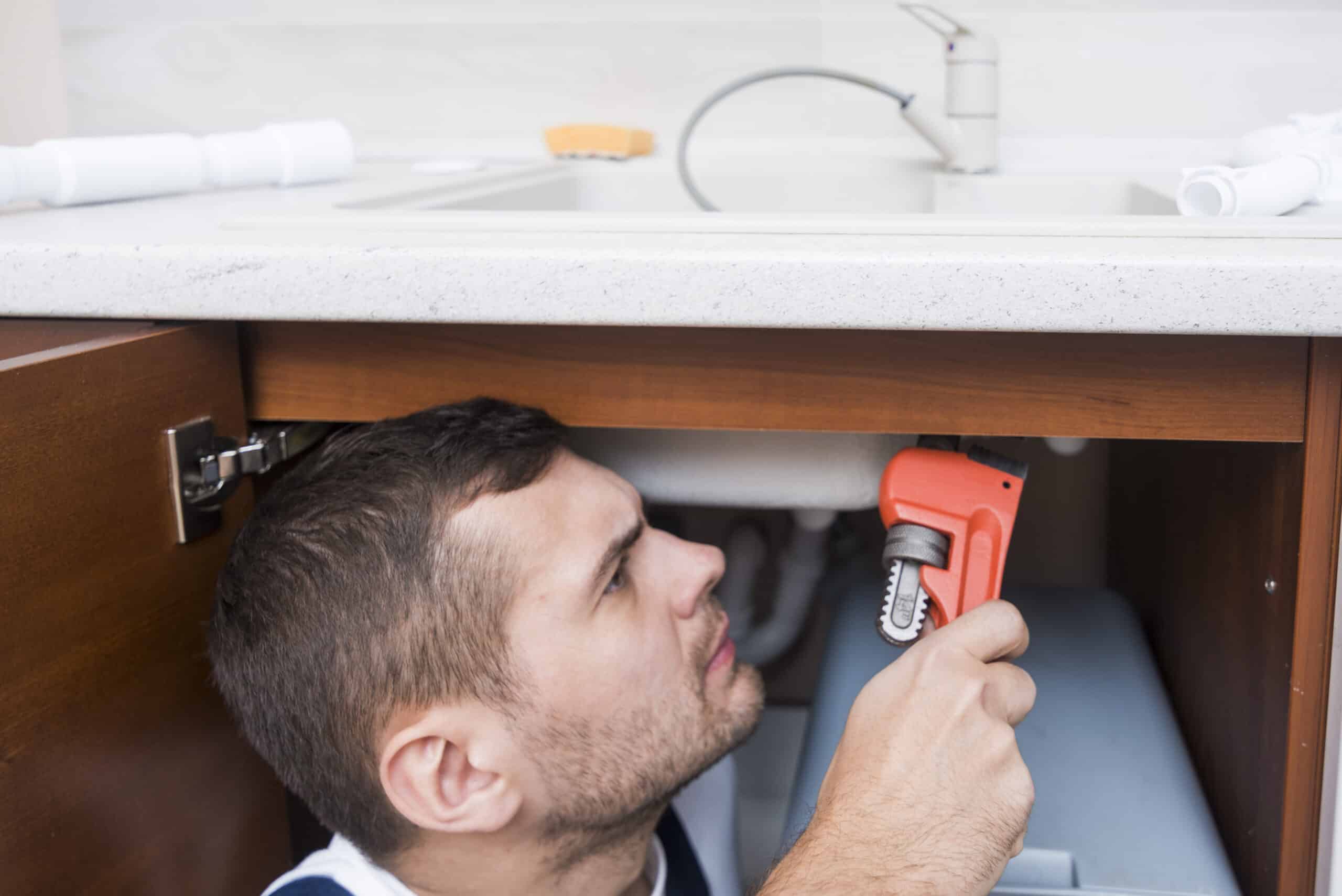 Sanitary technician using a wrench under a kitchen counter, illustrating Whirlpool dishwasher error code F4 drain fault