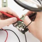 Technician using a multimeter to check a circuit board, illustrating LG dryer error code AE communication fault