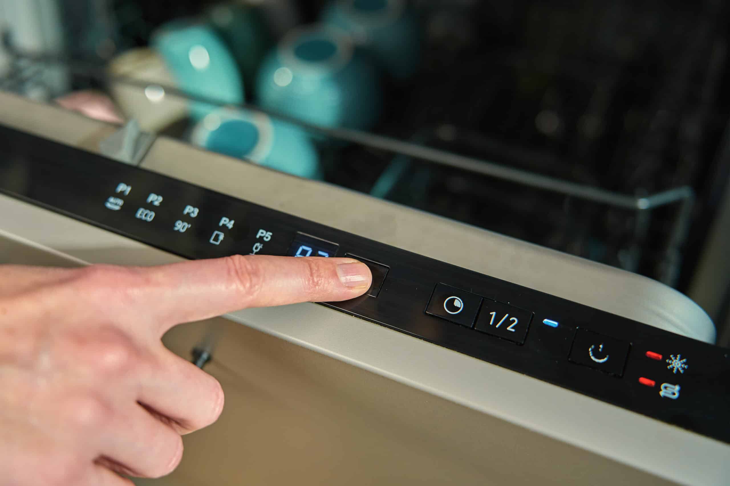 Close-up of a finger pressing a button on a dishwasher control panel that is not responding