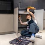 Technician inspecting piping under an appliance for pooled water, illustrating an LG dishwasher AE E1 leak error