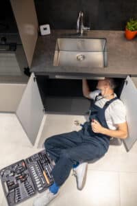 Technician fixing a garbage disposal unit under the sink, about to press the reset button