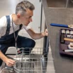 Technicien accroupi inspectant une fuite d'eau au socle d'un lave-vaisselle Whirlpool, code erreur F2