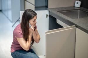 Woman listening near the kitchen sink trying to identify a humming garbage disposal noise