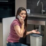 Person checking for a water leak near an appliance base, illustrating a Bosch dishwasher E15 leak sensor error
