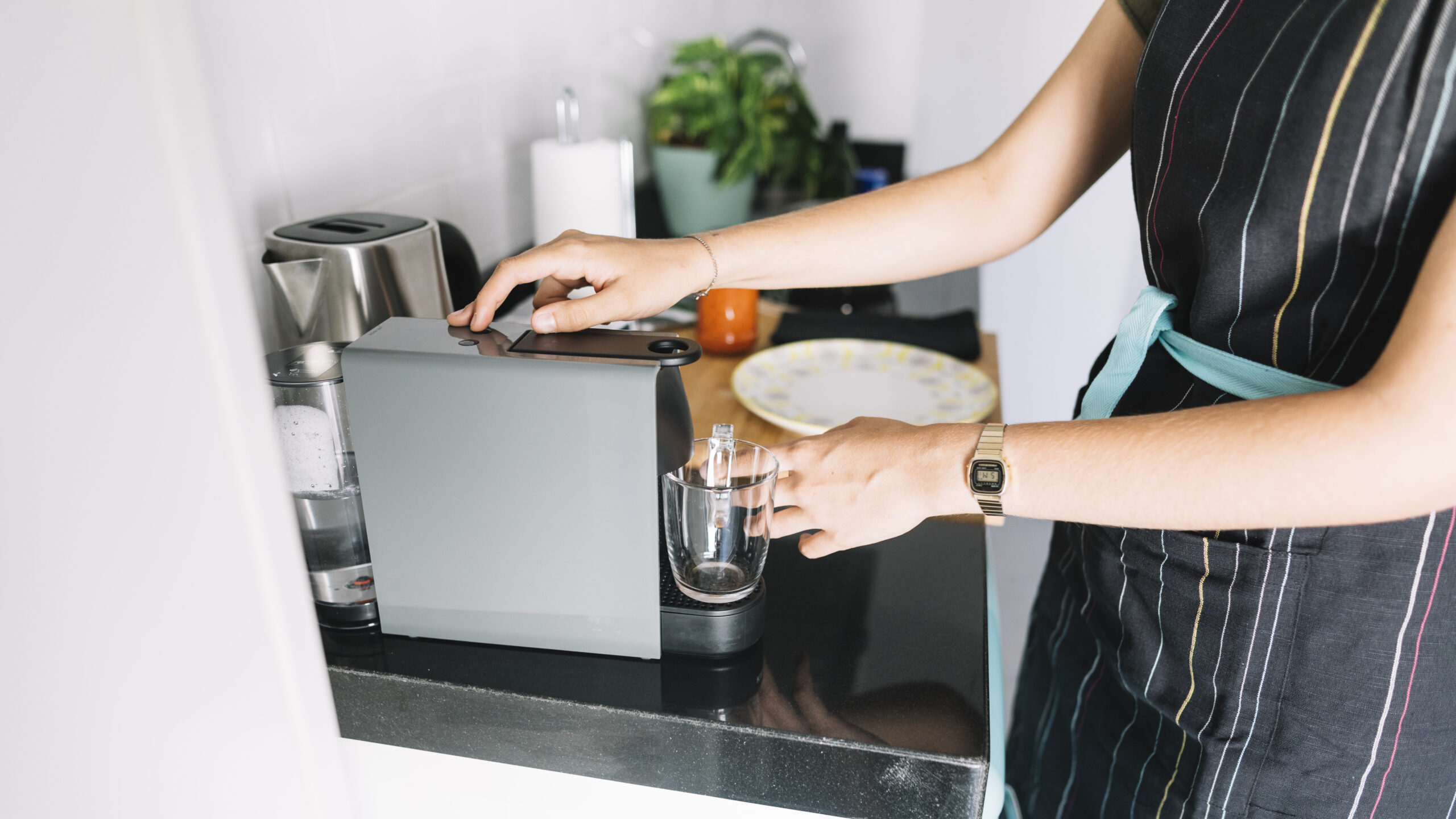 Person holding an empty glass under a countertop coffee machine in a home kitchen