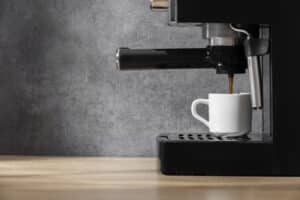 Black countertop coffee machine dispensing coffee into a white cup on a wooden kitchen counter