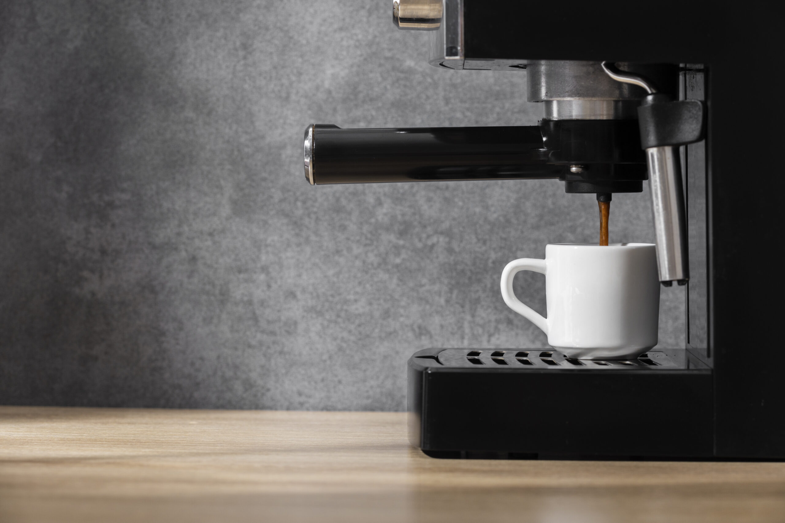 Black countertop coffee machine dispensing coffee into a white cup on a wooden kitchen counter