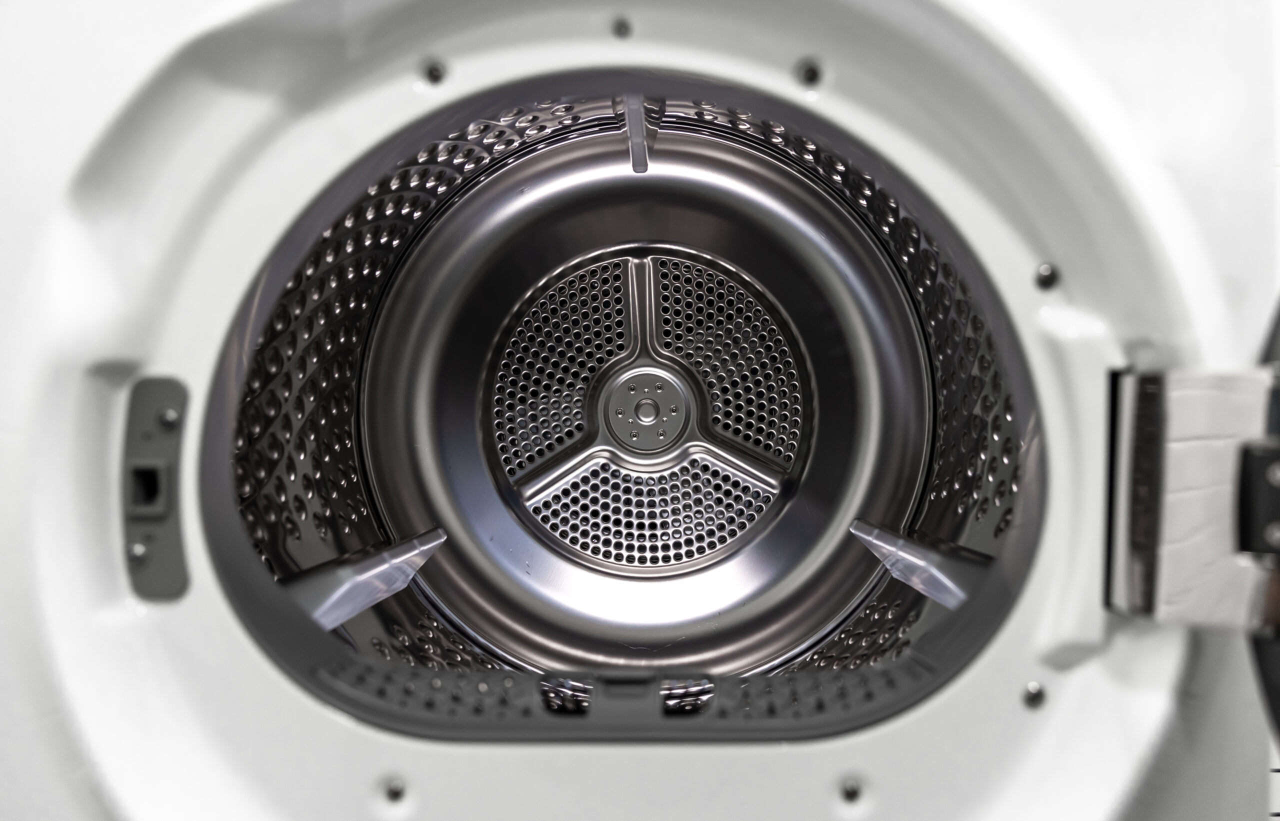 Open door of a white clothes dryer showing the empty stainless drum and its lifters
