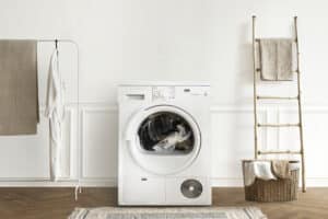 White front-load washing machine in a minimal laundry room with a drying rack and a wicker basket