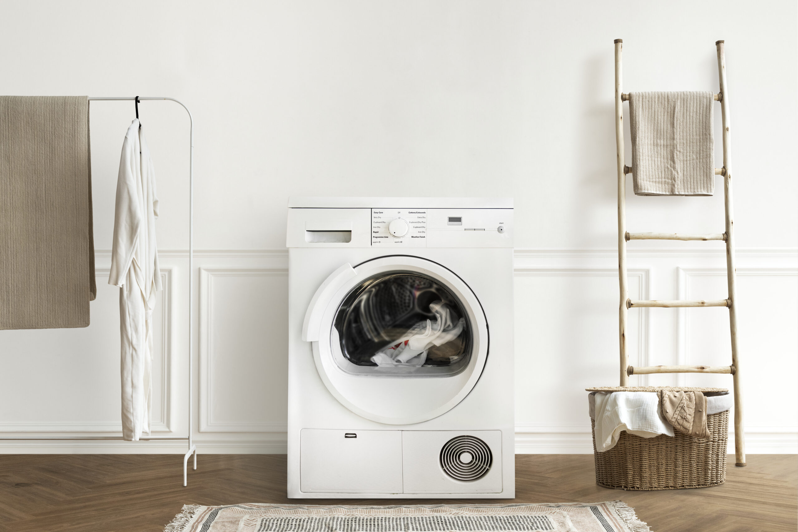 White front-load washing machine in a minimal laundry room with a drying rack and a wicker basket