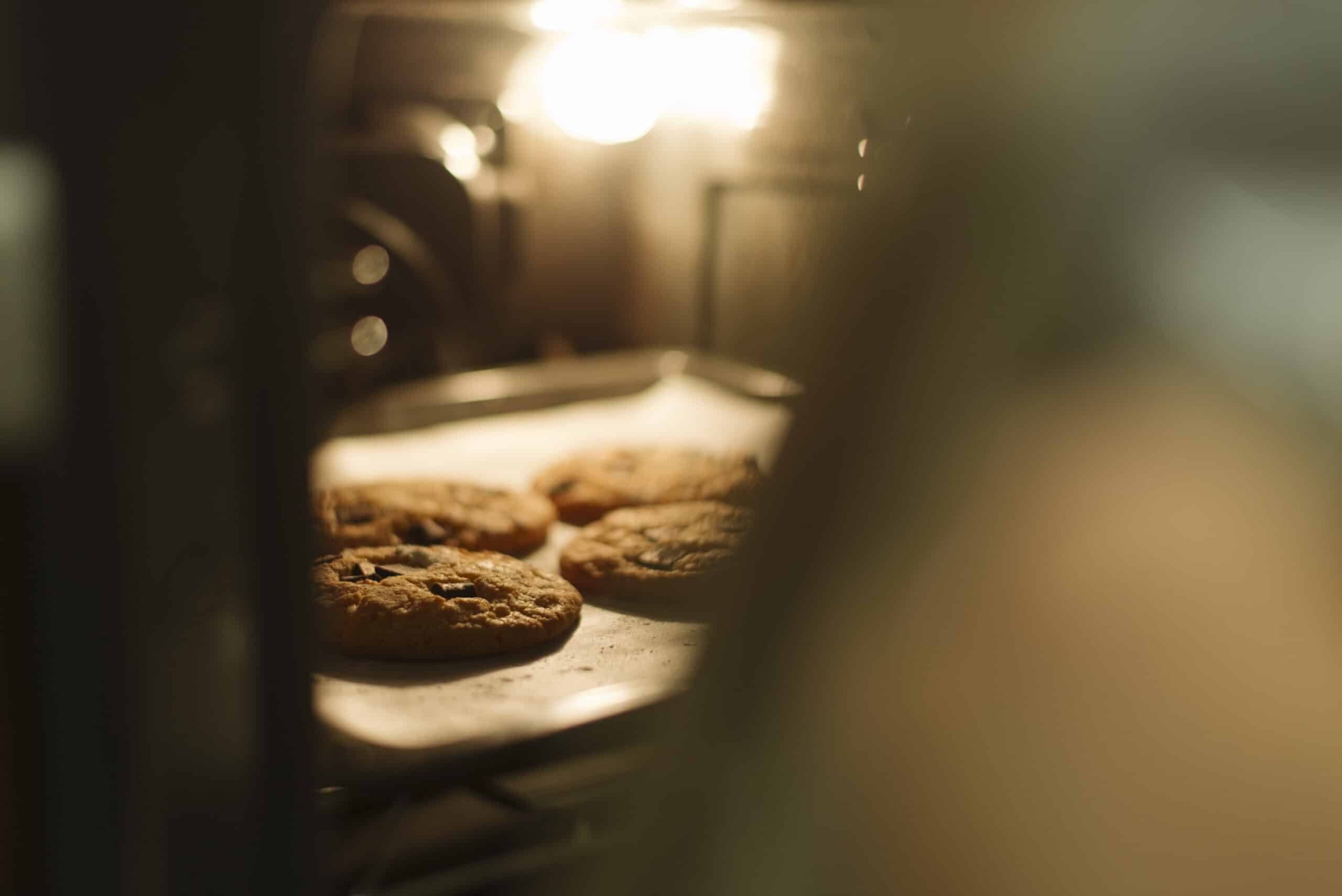 Tray of cookies baking inside an oven lit by its interior lamp